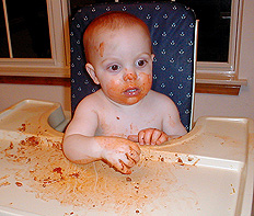 baby in high chair covered in spaghetti